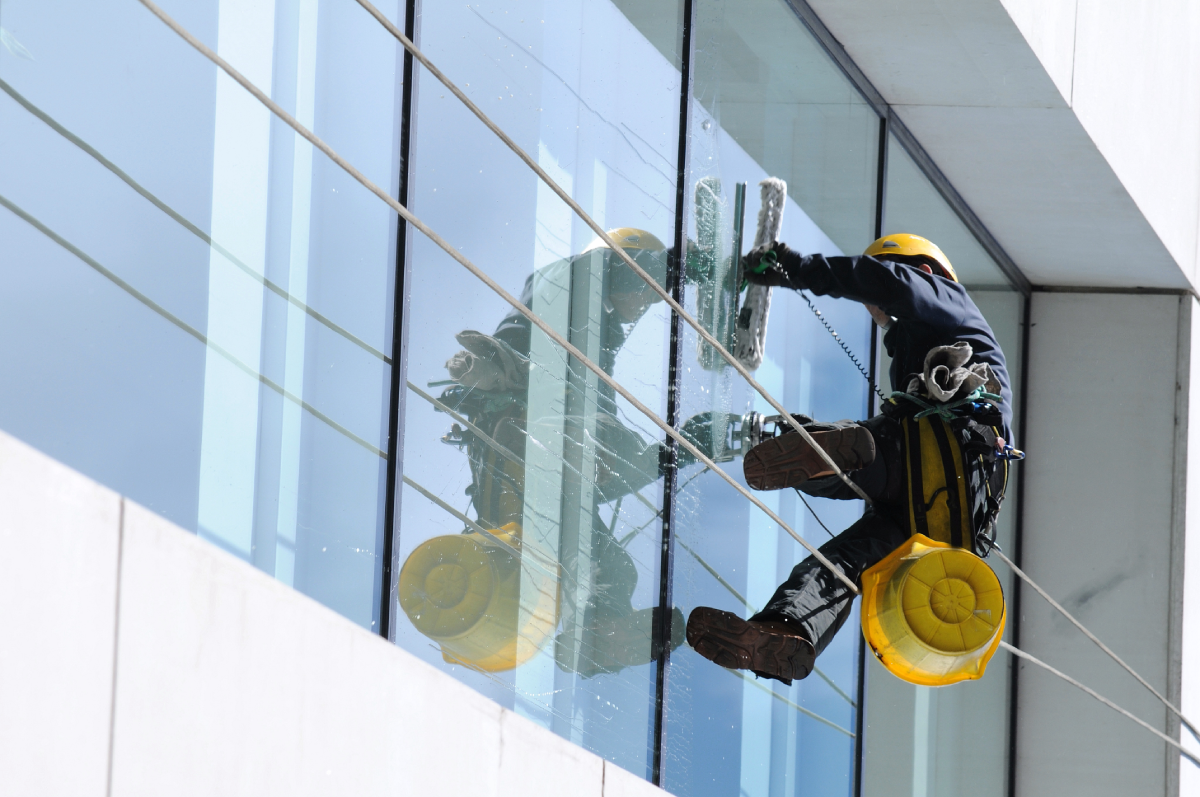 Window cleaner wearing safety gear cleaning a high-rise building’s glass facade using rope access.