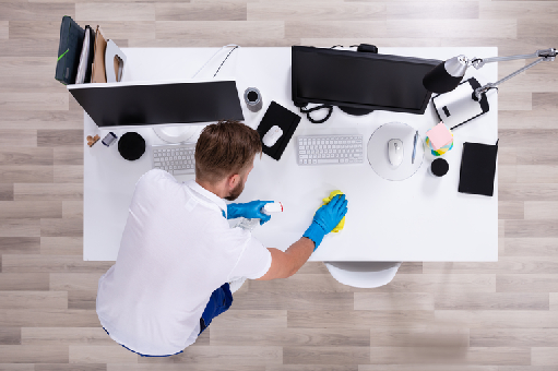 janitorial cleaning professional disinfecting office desk and workspace from top view