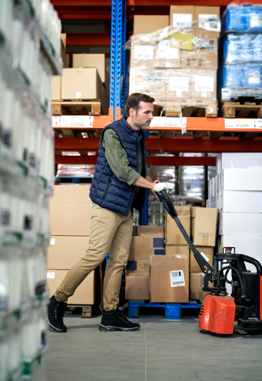 Warehouse worker using floor equipment near storage racks and pallets